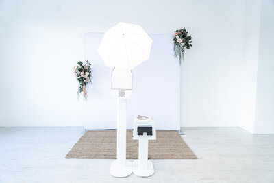 Photo booth and printer set up in front of white backdrop at wedding.