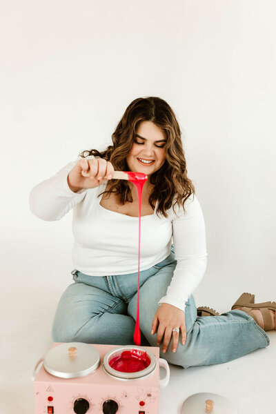 Licensed esthetician Macayla Hopper holding wax stick over wax warmer during body waxing prep in Hartselle studio