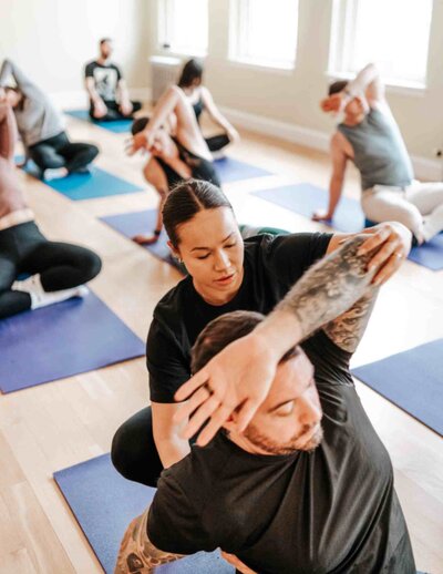 A breathwork instructor assisting a participant in an intercostal stretch, improving lung expansion and rib mobility for deeper breathing.