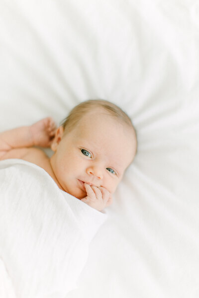 A newborn baby laying down on a white duvet with a white swaddle wrapped loosely around them