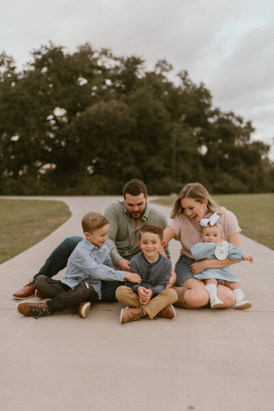 A family of 5 sitting on a pathway tickling each other. 