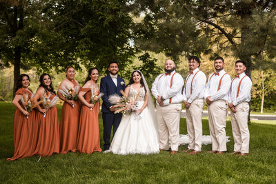 a wedding party of eight woman in orange rust dresses and men in tan pants with white shirt