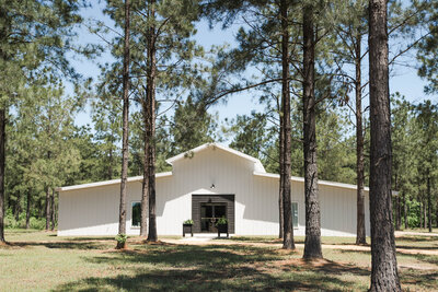 Modern western-style event barn with white exterior, wood accents, and large windows under blue skies.
