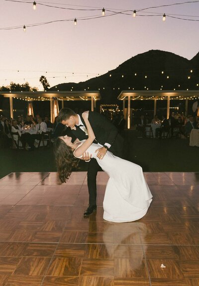 Groom photographing bride as she spins with bouquet in vineyard
