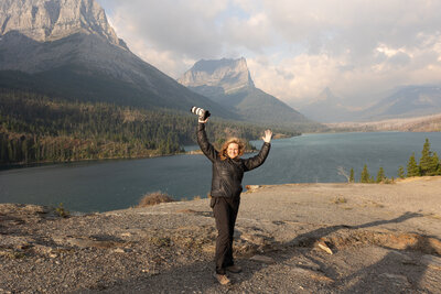 Female photographer holding camera above her head arms up in front of Glacier Mountain