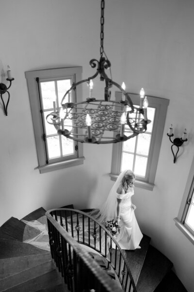 Bride walking down staircase under chandelier – black and white