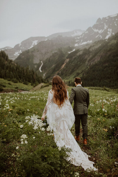 Bride and groom walk through a meadow of wildflowers on their Ouray elopement day