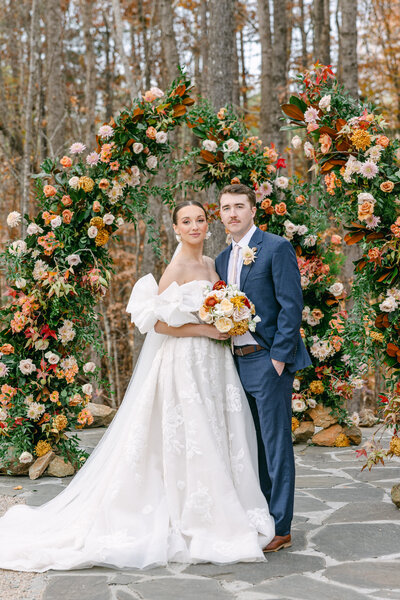 bride and groom posing by a floral arch