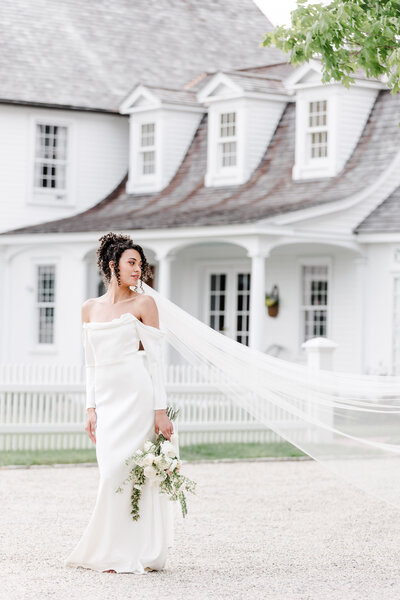 bride holding a bouquet and posing as veil flies in the wind