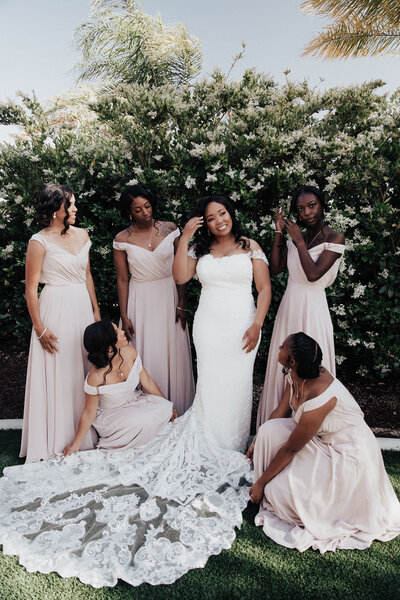 Bride posing with bridesmaids fluffing dress and looking at bride
