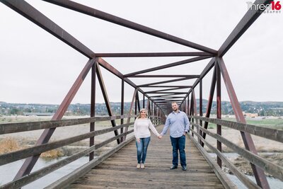 Engaged couple hold hands as they pose together on a bridge over the Santa Ana Riverbed at Yorba Regional Park