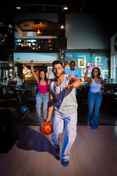 Group of six friends smiling and enjoying a night out, gathered around a table with drinks and food in a lively entertainment venue.