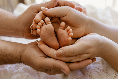 Close‑up of newborn feet cradled in parents’ hands during an in‑home session in Las Vegas.