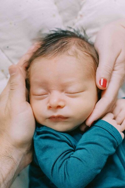 newborn baby boy's face being framed by his parent's hands