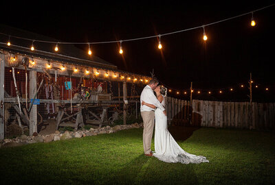 bride and groom kiss among bistro lights at night