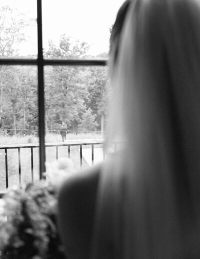 A bride and groom walk across a lawn in a documentary-style black and white photo.