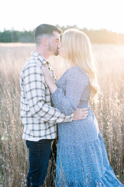 engaged couple kissing in field at sunset