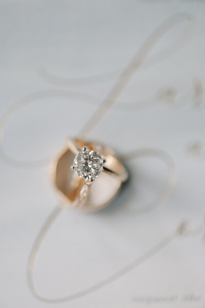 Bride and grooms gold wedding rings sit on top of their wedding invitation. Photo by Anna Brace, a wedding photographer in DSM IA. 
