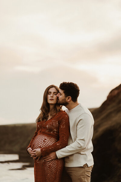 Maternity photoshoot in melbourne. Pregnant other in a field wearing a white dress that opens at the front showing her bare belly bump/ 30 weeks gestation. Hands are near her face as she embraces her growing body.