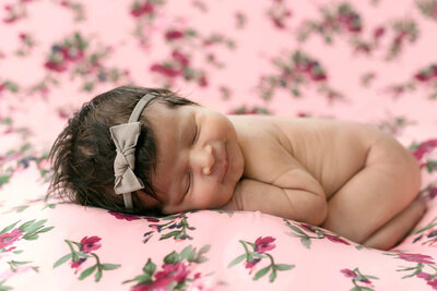 Posed newborn baby smiling on a pink floral blanket