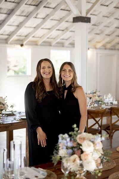 Two women smiling surrounded by laid wedding tables and floral arrangements