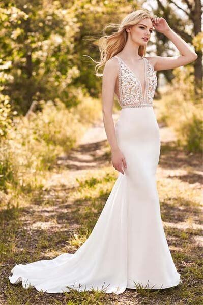 Mikaella Style 2297 is a stunning fitted Crêpe wedding dress with a sheer Guipure Lace bodice. Mesmerizing Lace Trim outlines the plunging neckline, waist, and V-shaped arm holes on this gorgeous gown. Each piece of lace is carefully and perfectly pinned and sewn by hand, so we can always uphold exceptional quality.