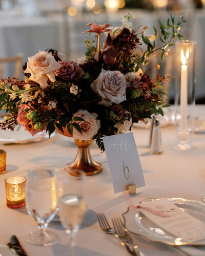 Moody floral centerpiece with blush and mauve roses surrounded by glowing candlelight on a table set for a romantic wedding reception at the Renaissance Hotel in Pittsburgh.