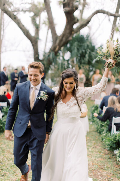 Newlyweds walk joyfully down the aisle after an outdoor forest ceremony, kicking off a full wedding weekend planned by The Eventful Gals.
