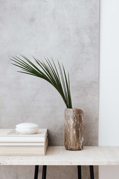 marble vase with palm leaf beside a stack of books and in front of a paster wall