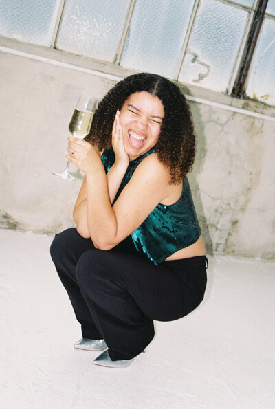 Photo of Catryce smiling and crouching down with a bottle of champagne
