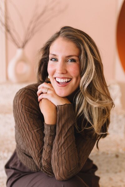 Shannon Bills smiling warmly in a chic brown outfit, embodying a confident and approachable vibe against a modern neutral backdrop