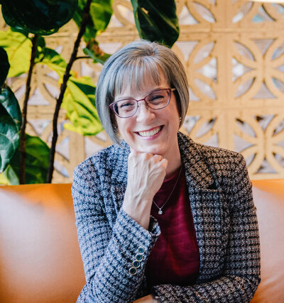 Jayne sitting on a leather couch, hand gently resting on her chin, smiling