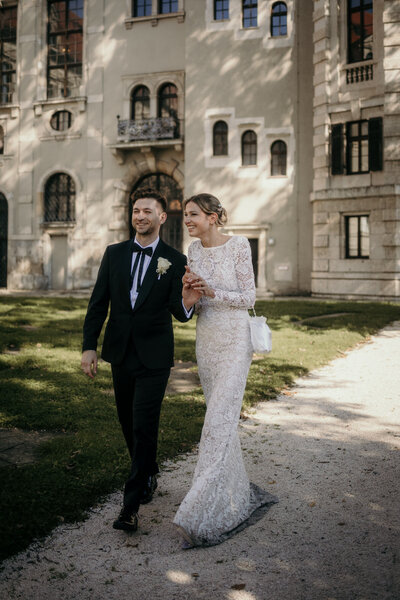 Bride and groom walk outside their wedding venue holding hands, chatting relaxed.