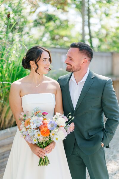 A bride and groom smile at one another at their wedding. 