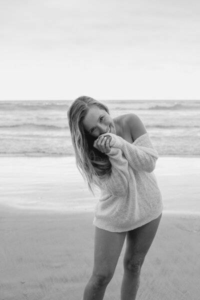 Woman on beach wearing sweater smiling with hand close to face