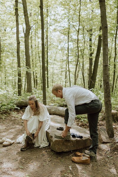 bride and groom putting on hiking boots together in the woods while getting ready for their elopement in Wisconsin