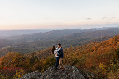 A couple kisses while sitting on a porch, greenery behind them.