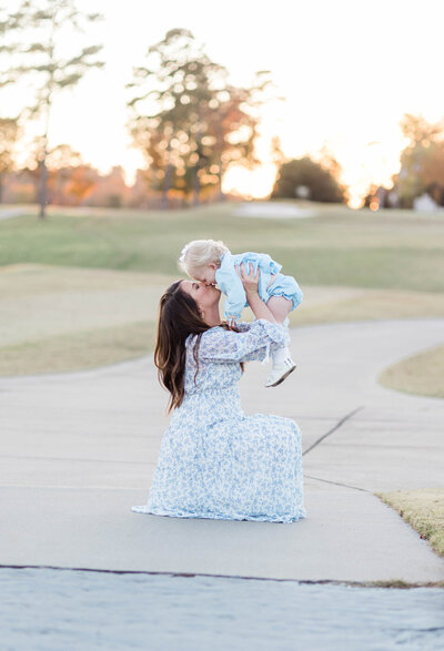 Mom holding and kissing toddler on golf course with sunset in the background