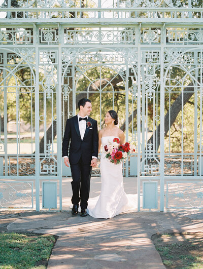 Bride and groom walking hand-in-hand in front of a decorative garden gate during a stylish Austin wedding, planned with elegance and personality.