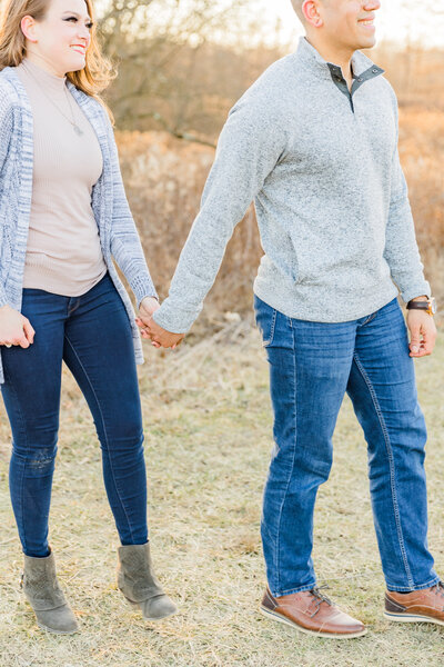 guy in grey sweater and girl in tan shirt holding hands and walking through a field in ohio