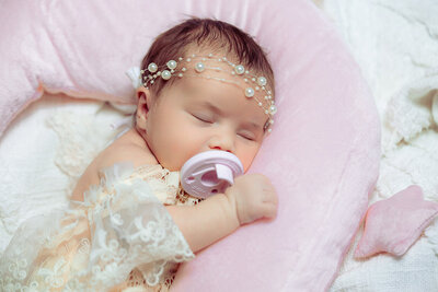 Salt Lake City newborn photographer capturing a baby in a lace outfit on soft pink bedding. Moonlit Photo Utah newborn photography with delicate details and heirloom styling.