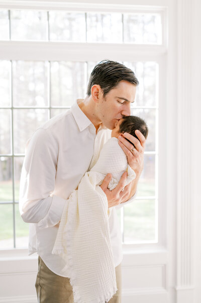 Dad holds newborn son wrapped in ivory blanket during in-home newborn session