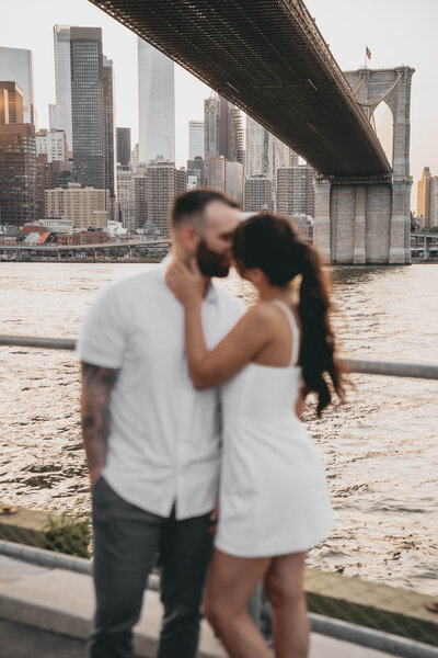 man and woman kissing in front of water with city in the background
