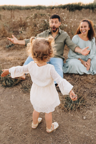Dad sits with open arms as his daughter runs towards him with her arms open. 
