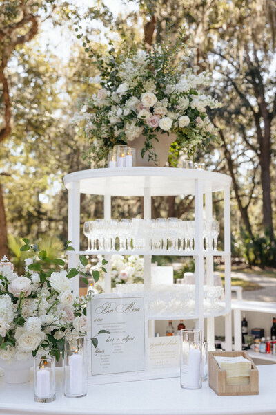Custom outdoor bar with floral arrangement on bar top and on circular barback — part of a bespoke wedding design by The Eventful Gals.