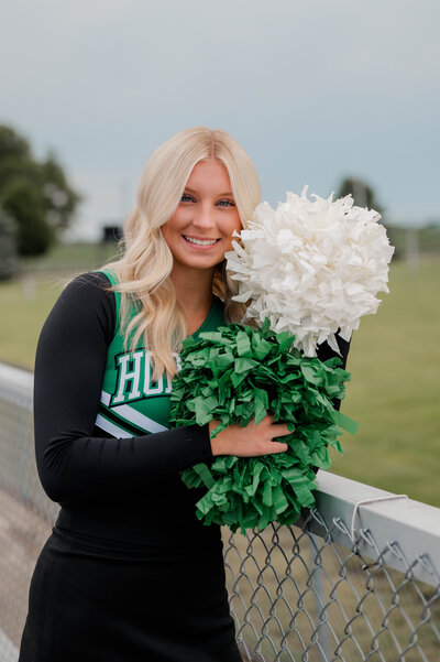 High school pommer poses for the camera with pom poms on the football field.
