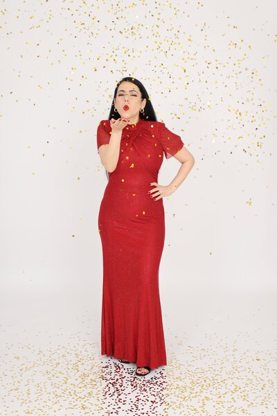 Vancouver boudoir photographer Gina Spanos in a red gown surrounded by gold confetti, celebrating confidence and beauty at her Burnaby studio.