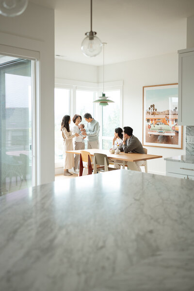 A family gathered in their light-filled Orange County home during an at-home photo session, holding their newborn near the dining table.