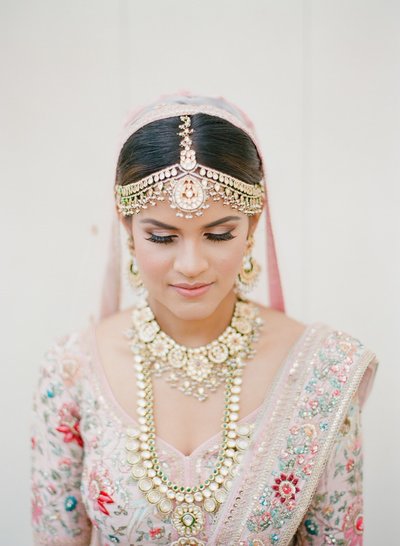 Bride wearing traditional maang tikka gold in a pink dress with pink veil for her wedding day in San Diego