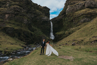 A man and woman stand hand in hand in front of an Icelandic waterfall